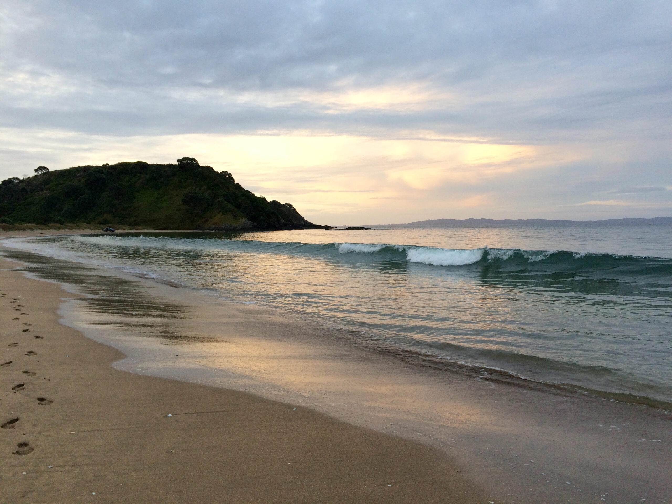 Peaceful sunrise at Taipa Beach in Northland, New Zealand, with gentle waves and a scenic headland in the distance.
