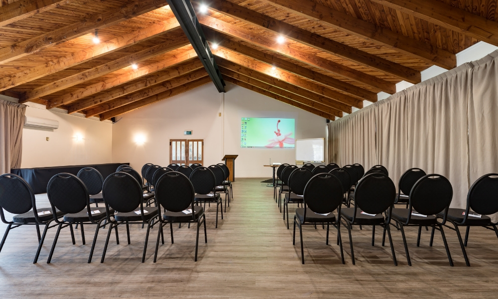 Spacious conference room with theatre-style seating, high wooden ceilings, and projector setup at Taipa Beach Resort.