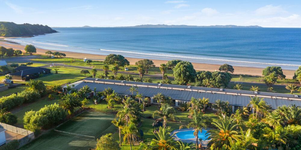 Aerial view of beachfront resort with pool, tennis court, and ocean.