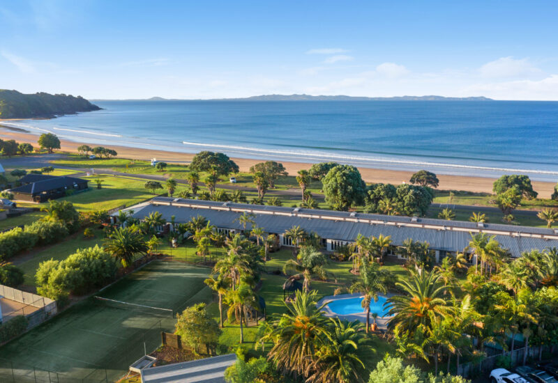 Aerial view of beachfront resort with pool, tennis court, and ocean.