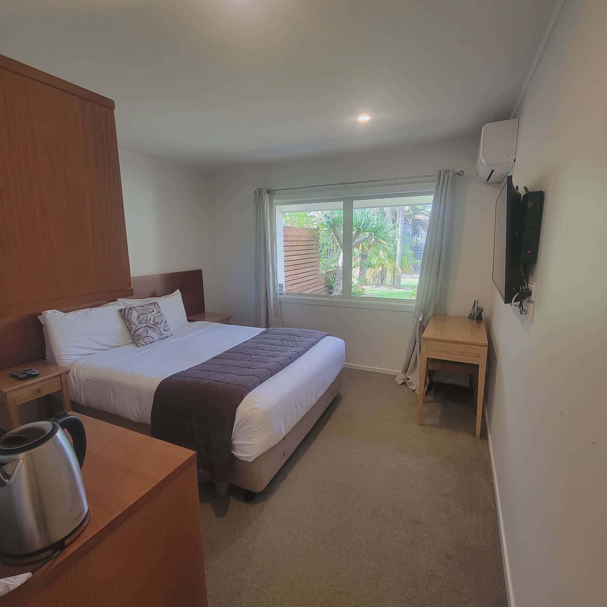 Taipa Beach Resort guest room with queen bed, air conditioning, workspace, and garden view window.