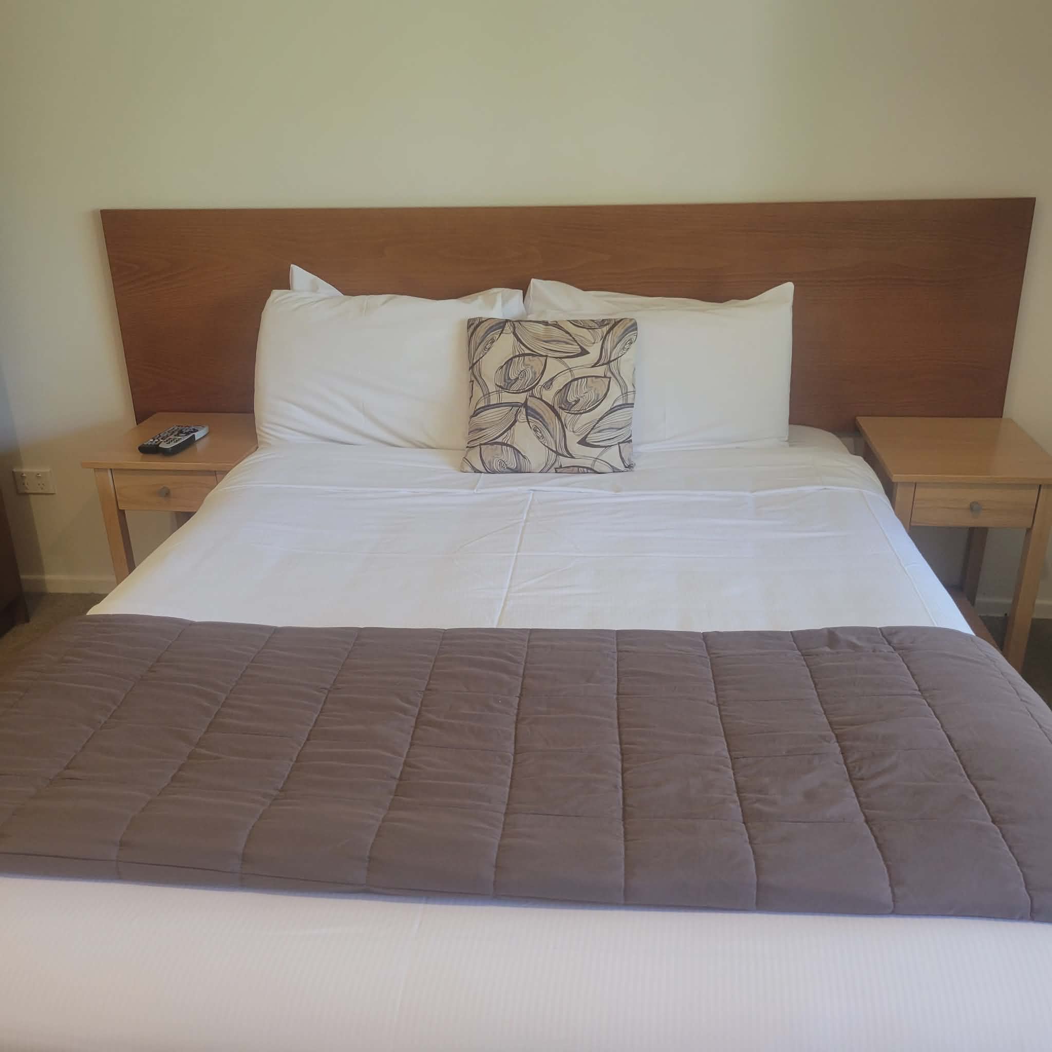 Queen bed at Taipa Beach Resort with crisp white linens, bedside tables, and modern headboard.