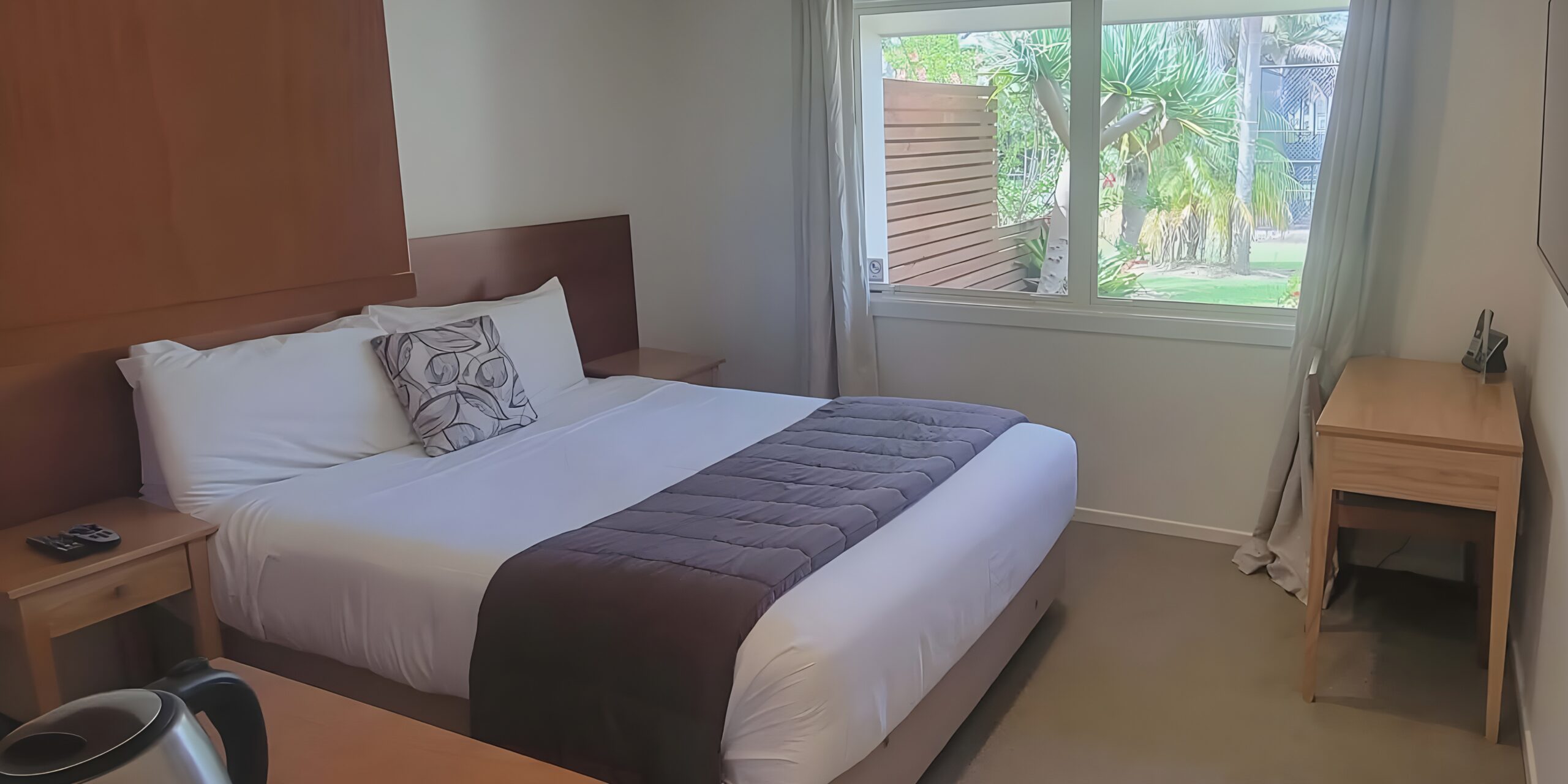 Bright bedroom at Taipa Beach Resort featuring queen bed and leafy garden outlook.