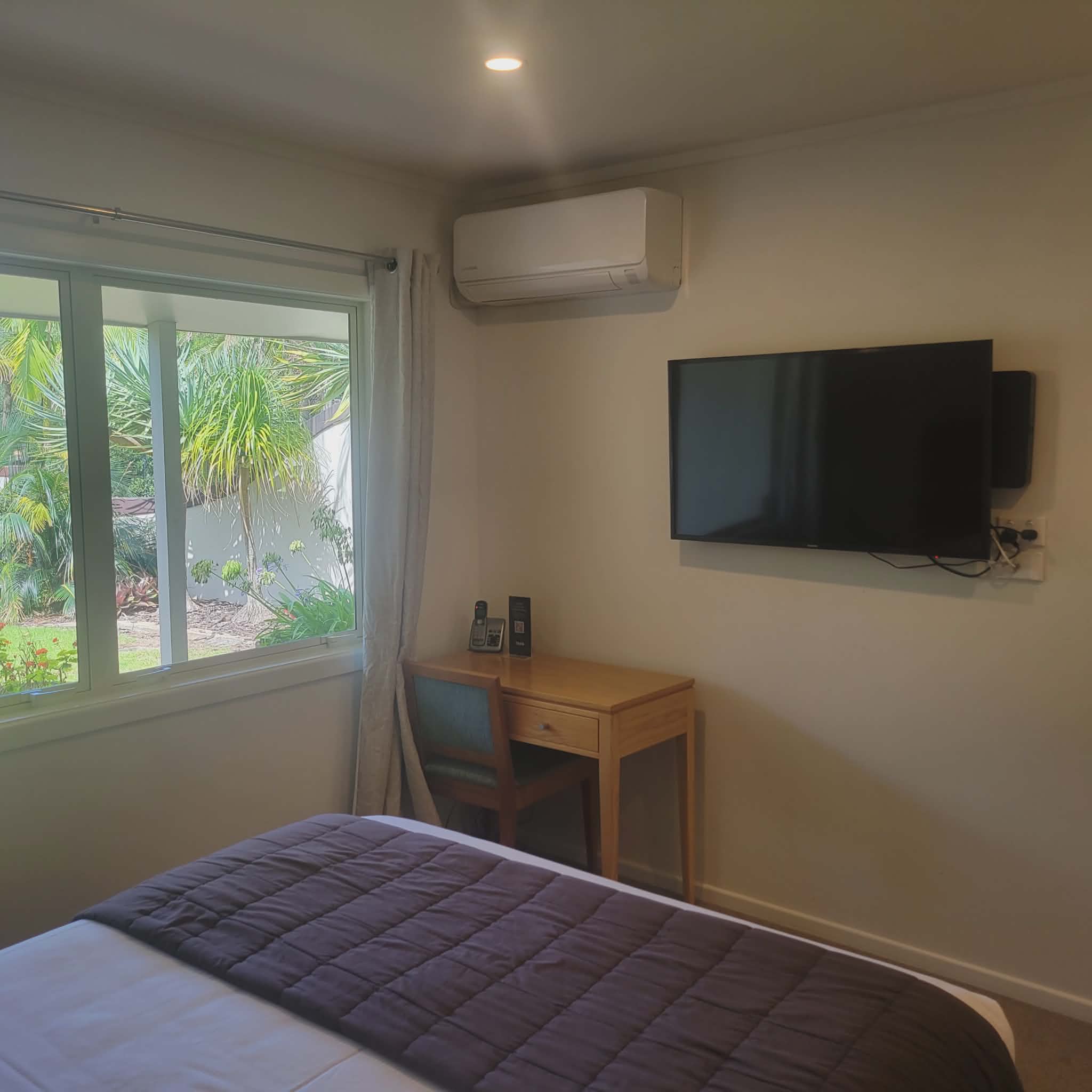 Taipa Beach Resort guest room with wall-mounted TV, air conditioning, desk, and garden view window.