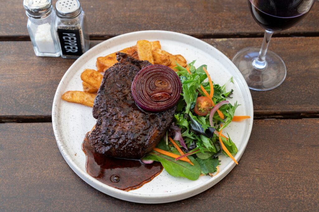 Scotch fillet steak with fries, fresh garden salad and caramelised red onion served at Taipa Beach Resort Restaurant in Doubtless Bay, Northland.